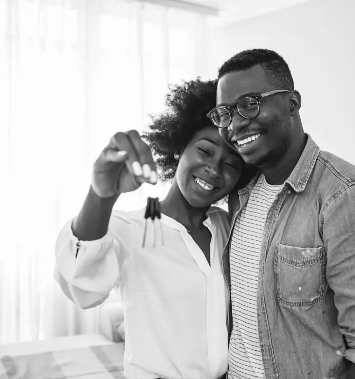 A young, happy couple with the woman holding up a pair of keys to their new home