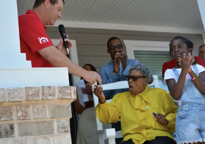 HistoryMaker employee handing an item over to an elderly lady sitting on a chair on the balcony of a home