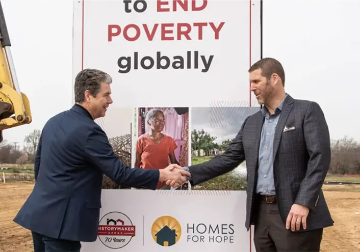 Two men shaking hands in front of a kiosk with a message stating to END POVERTY globally